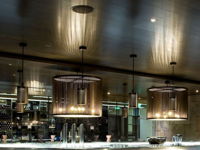 Archisio - Illuminazione Chary - Progetto Bergresort werfenweng - arch L Bellini - sospensione 135 h 90 cm composta da fasce verticali in metallo bronzato doppia sorgente luminosa